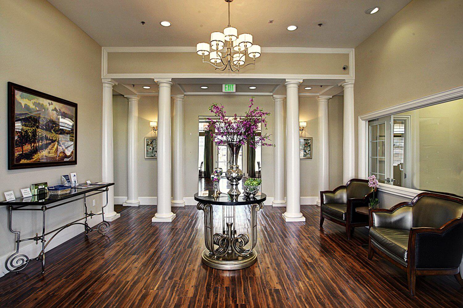 Elegant lobby with chandeliers and floral centerpiece on polished wood floors.