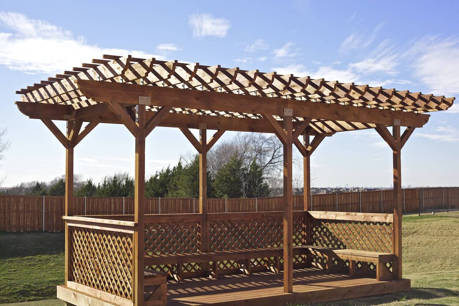 Wooden pergola with lattice panels in an outdoor setting.