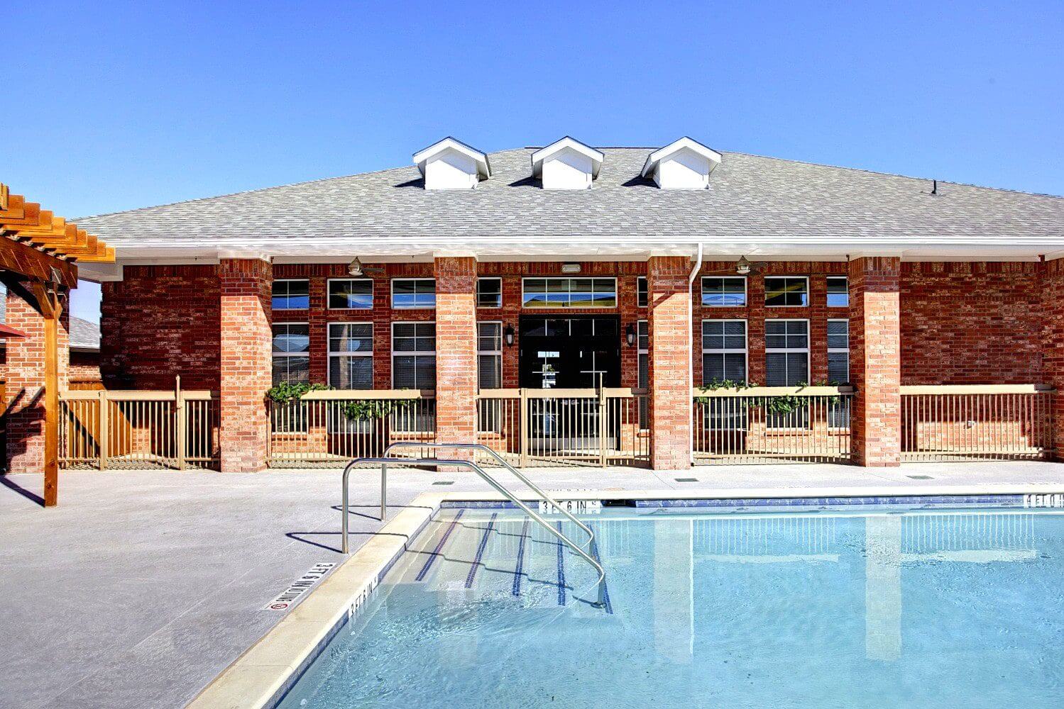 Modern brick building with large windows beside a clear swimming pool.