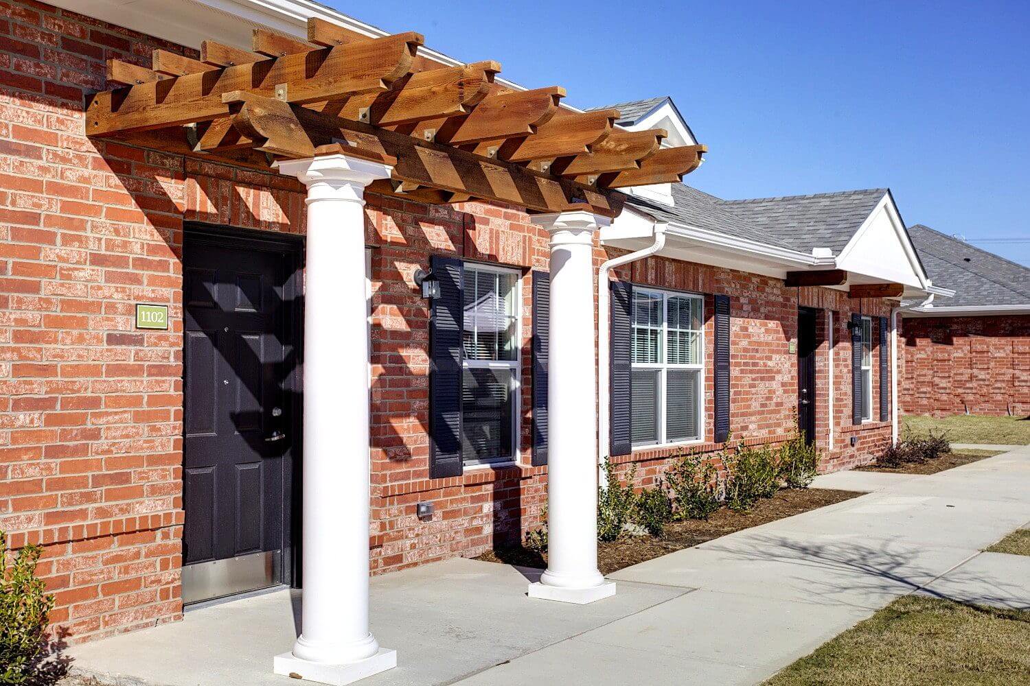 Brick house with white columns and wooden pergola on the porch.