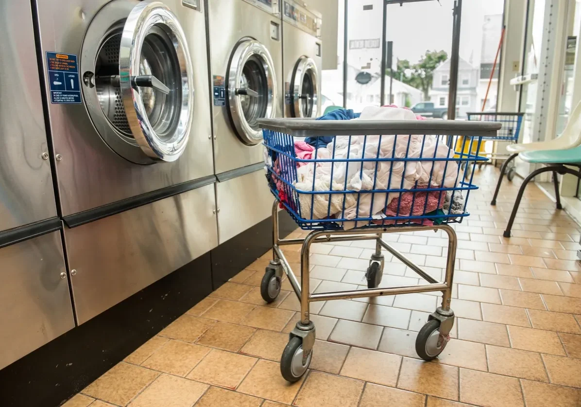 Laundry basket on wheels in front of washing machines at a laundromat.