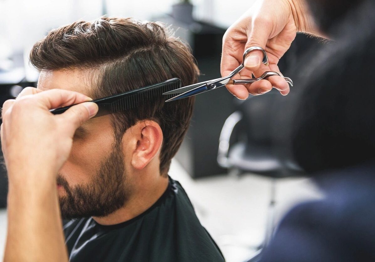 A barber cutting a man's hair with scissors and a comb.